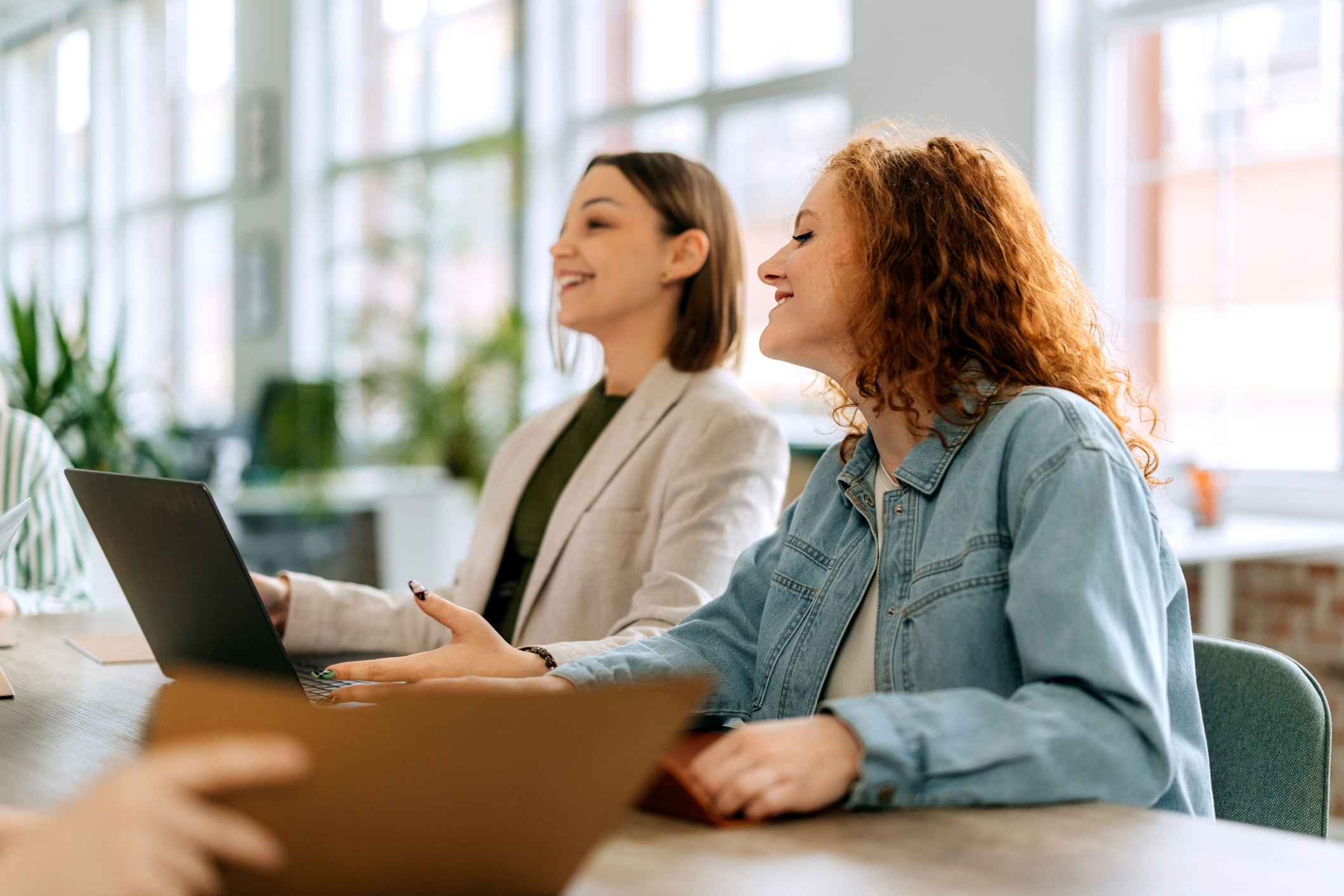 Two colleagues smiling and collaborating around a laptop in a bright office